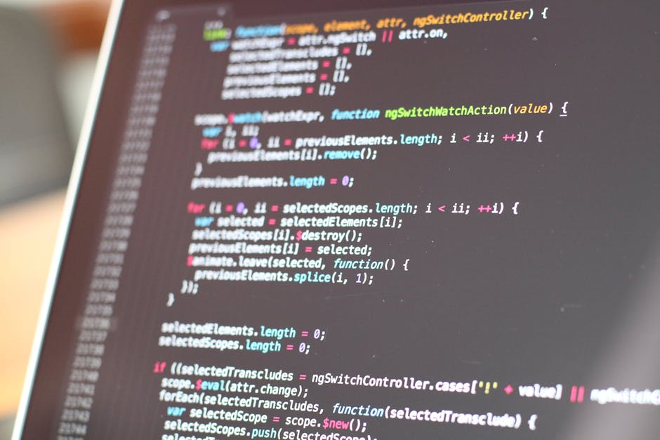 A close-up of a laptop screen displaying colorful lines of programming code, suggesting a workspace for a software developer. The monitor shows syntax-highlighted text with various commands and functi