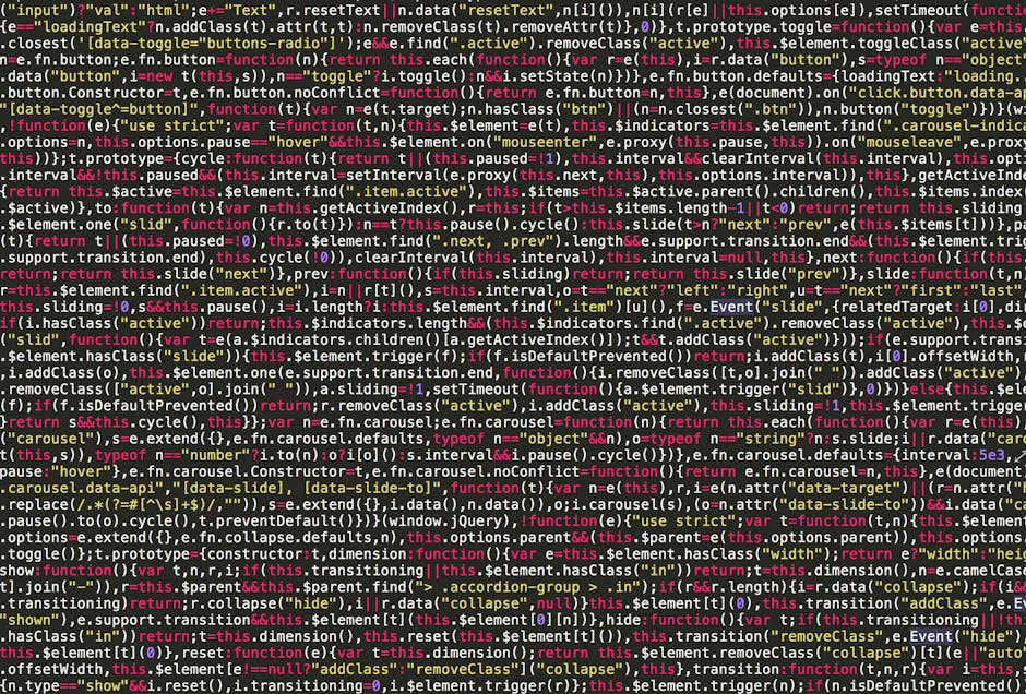 A close-up of a laptop screen displaying colorful lines of programming code, suggesting a workspace for a software developer. The monitor shows syntax-highlighted text with various commands and functi